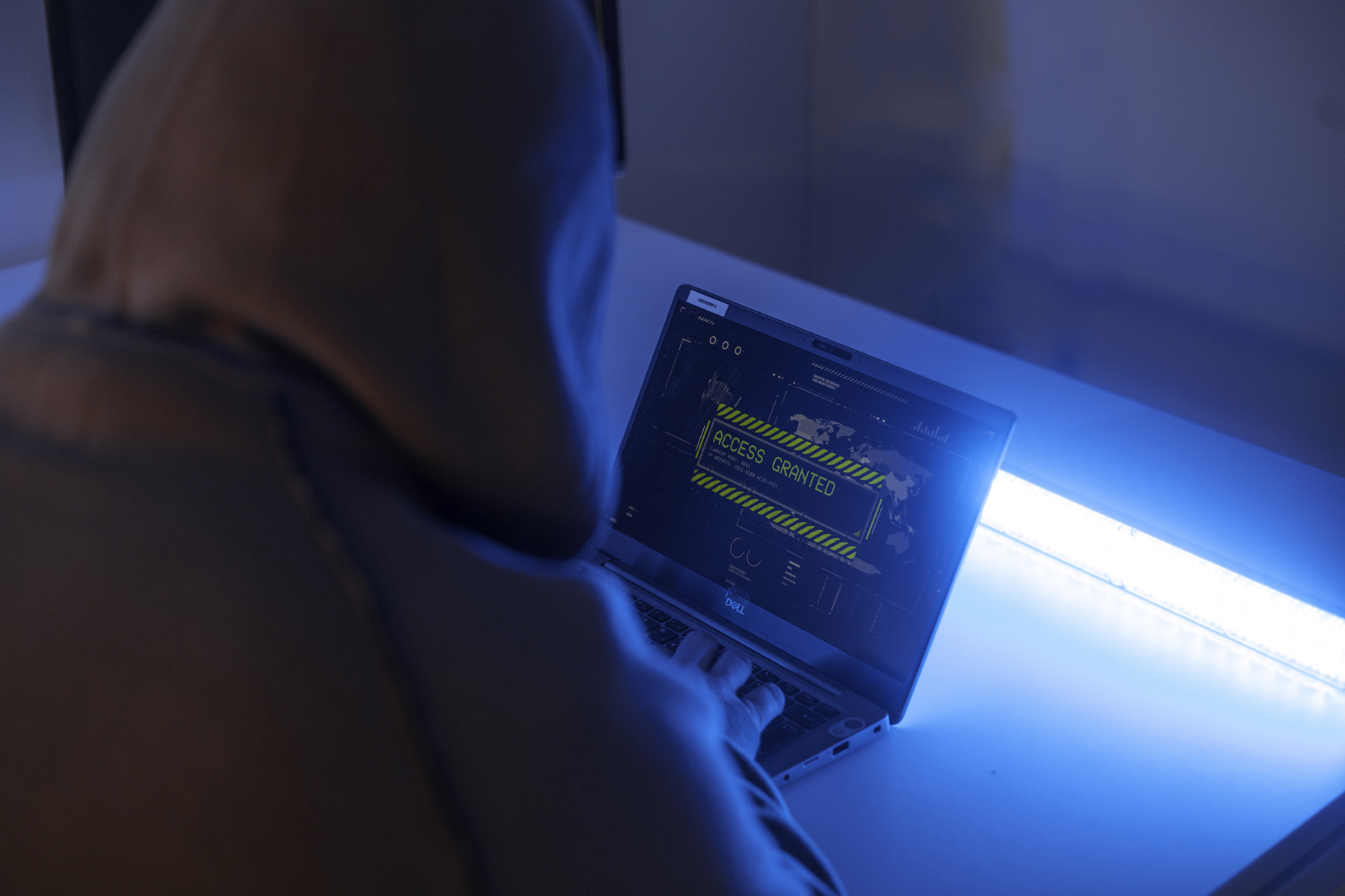 Person with a hood analyzing data on his computer. The colors are dark