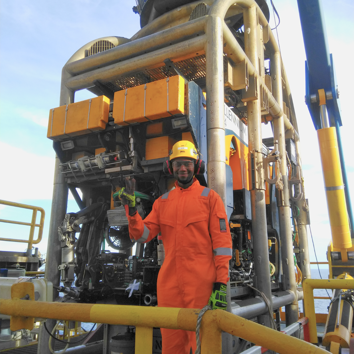 Salia en combinaison orange et casque de protection, devant un équipement industriel lors de sa mission offshore.